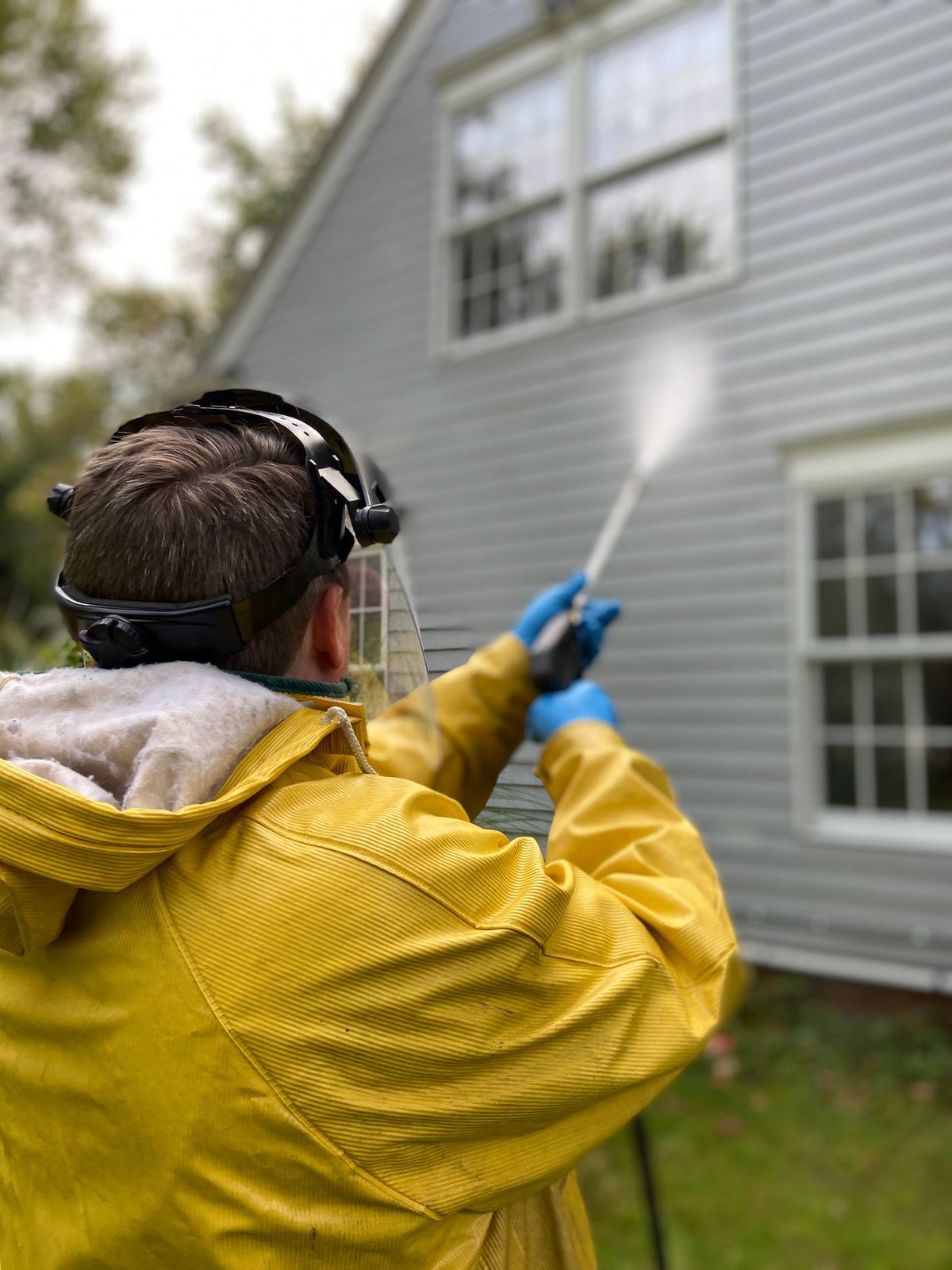 Technician soft-washing house siding with a pressure washer